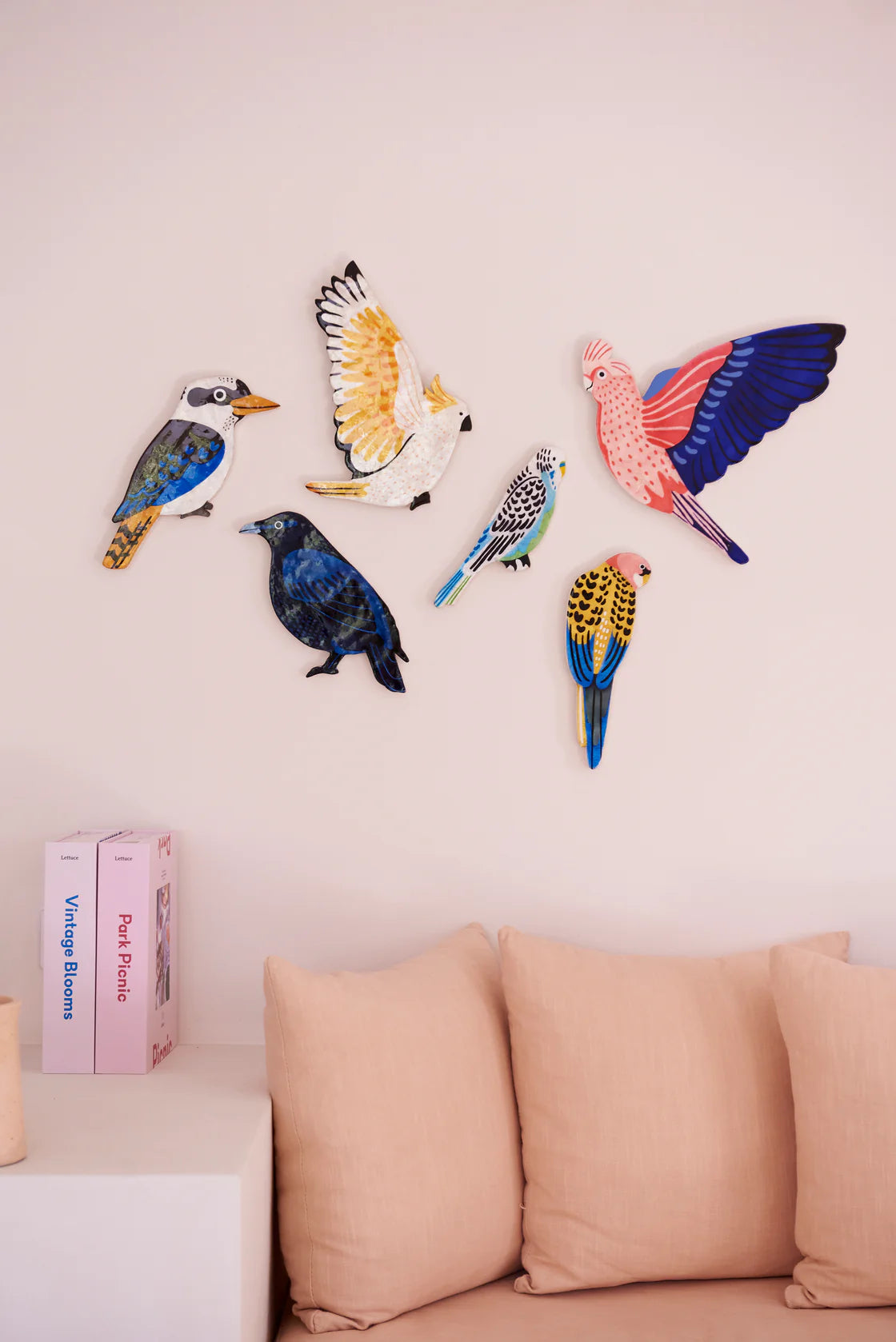 Colorful bird-shaped wall decorations on a light pink wall above a beige sofa.