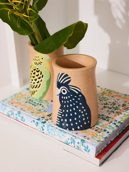Ceramic vase with a chicken design on a stack of books with another vase in the background.