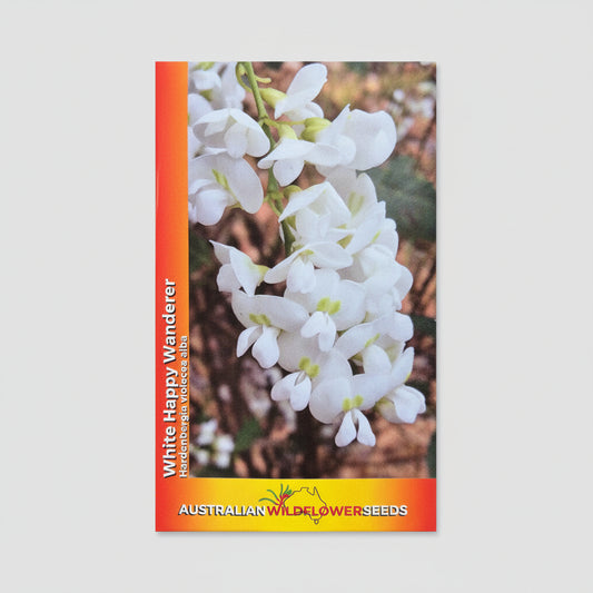A seed packet for 'White Happy Wanderer' native flowers from Australian Wildflower Seeds, featuring a photo of white flowers on a brown background, placed on a textured beige surface.